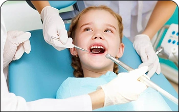 Pediatric dentist performing a gentle oral examination for a child in a dental chair.